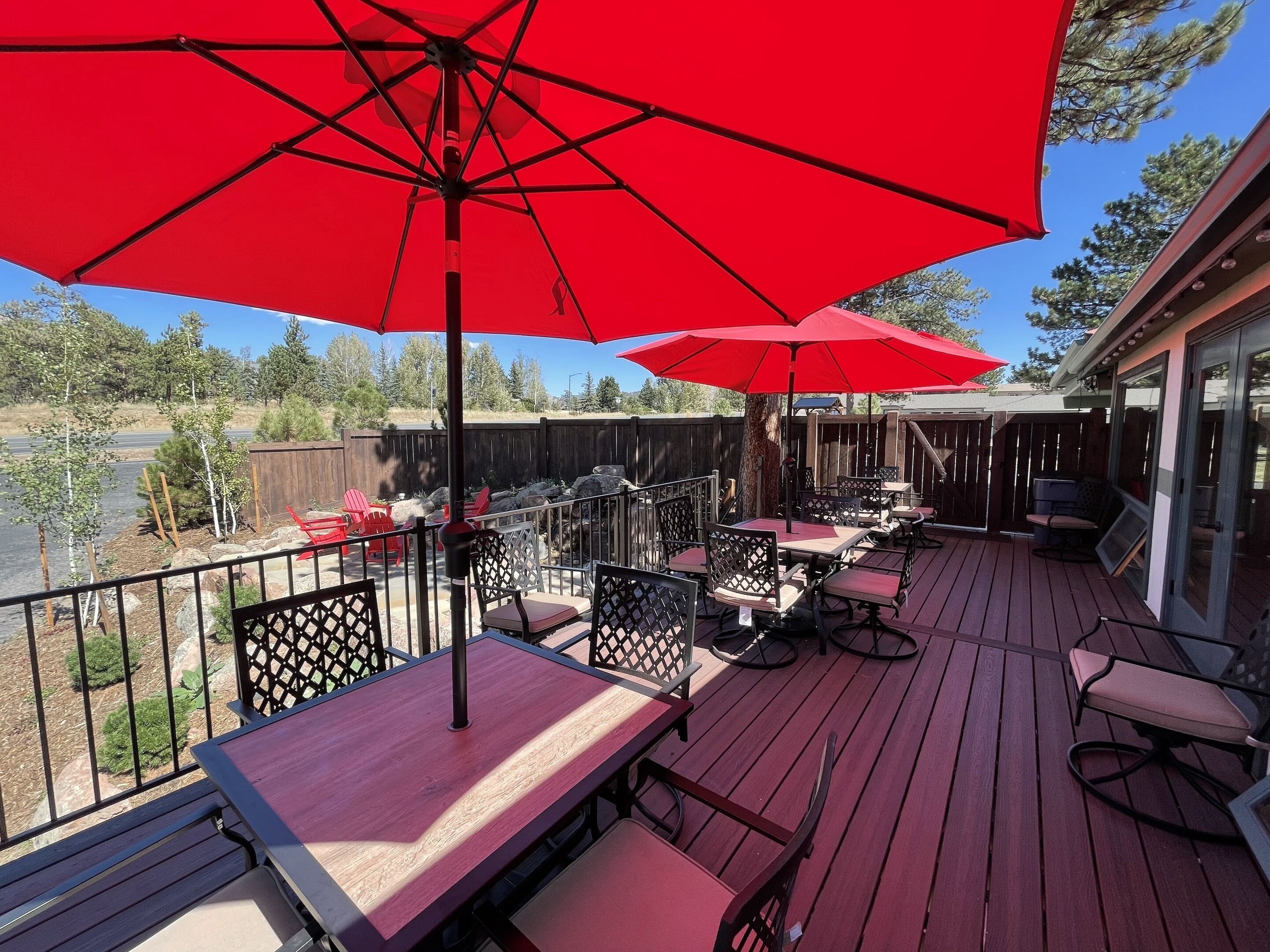A deck with outdoor seating, red umbrellas, and a view of a lake.