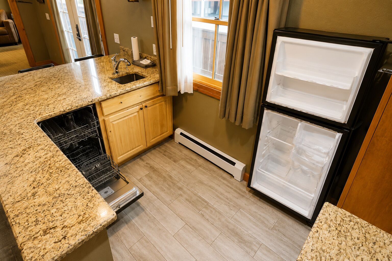 A kitchen with granite countertops, a built-in dishwasher, a double-door refrigerator, wooden cabinets, and a window with curtains.