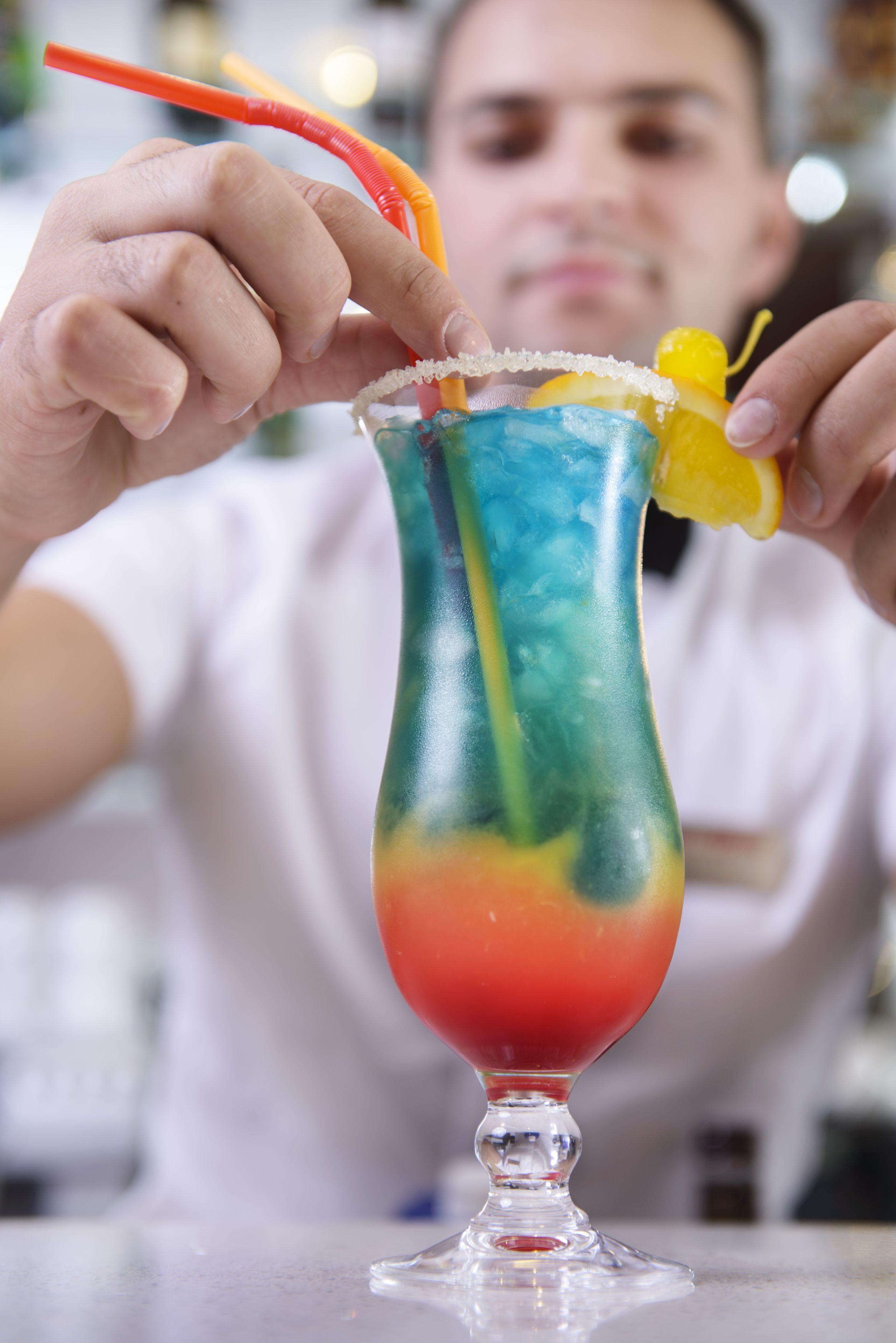 A colorful cocktail in a tall glass with a salted rim and a lemon twist garnish.