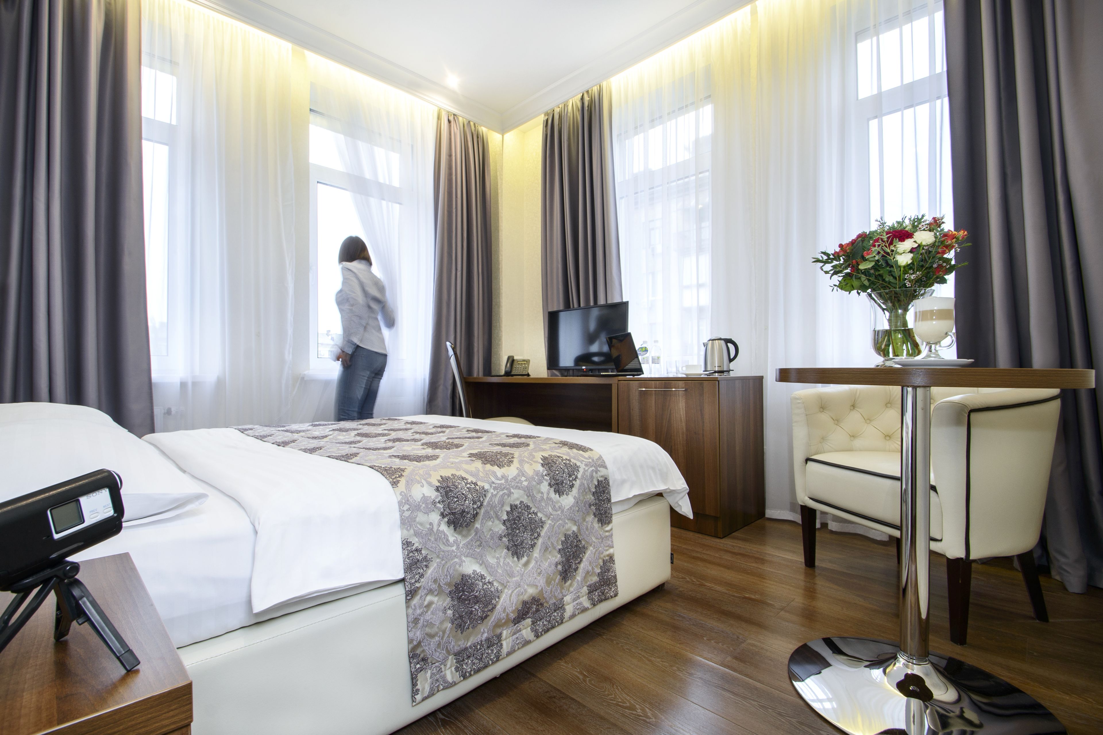 A hotel room with a bed, a desk, a chair, a TV, and a vase with flowers.