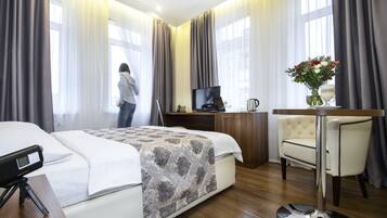 A hotel room with a bed, a desk, a chair, a TV, and a vase with flowers.