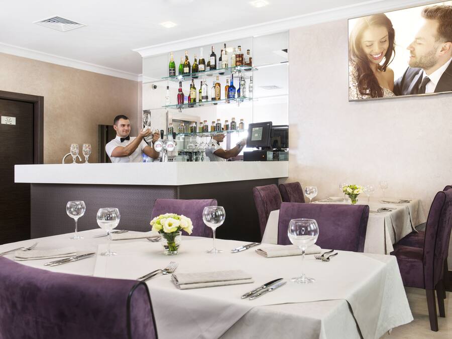 Un restaurant doté d’un bar, de chaises recouvertes d’un tissu violet et de nappes blanches.