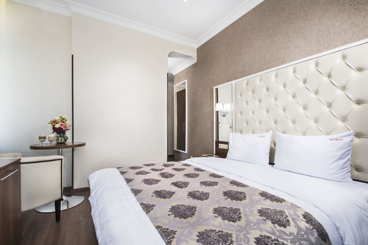 A hotel room with a large bed, a bedside table with a vase of flowers, and a mirror on the wall.