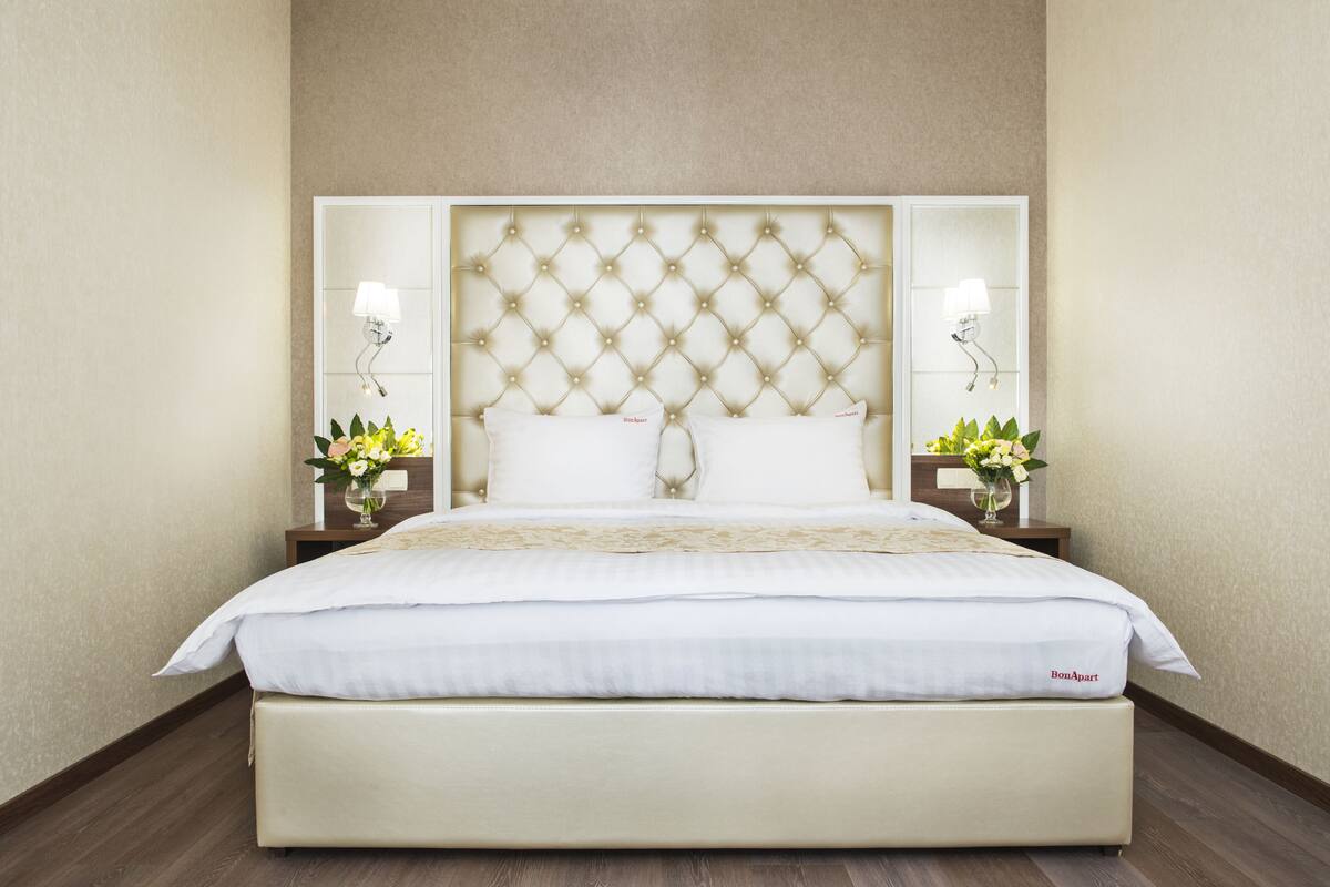 A large bed with a tufted headboard, two bedside tables with lamps, and a floral arrangement on each table.