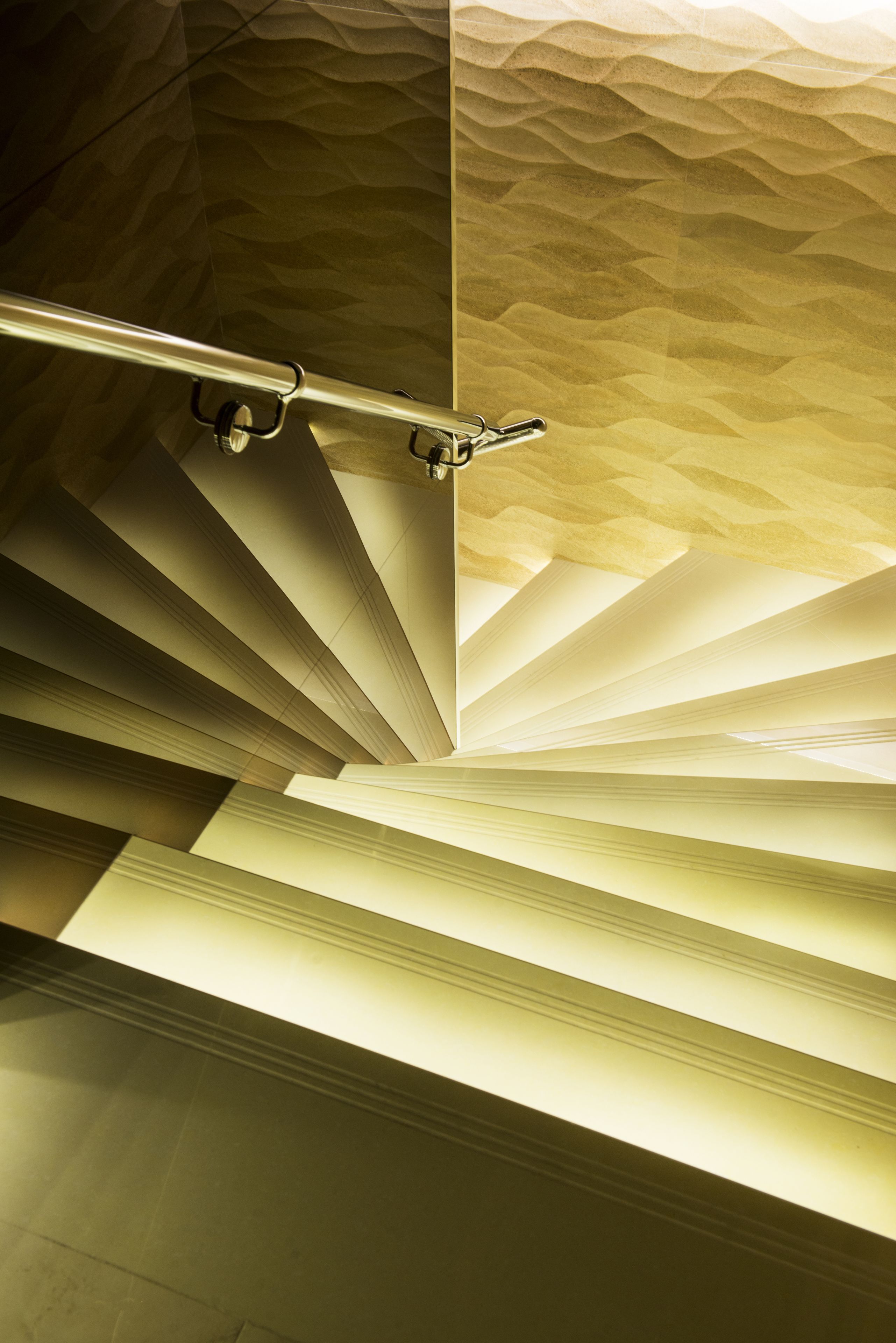 A staircase with a textured wall and a metal handrail.