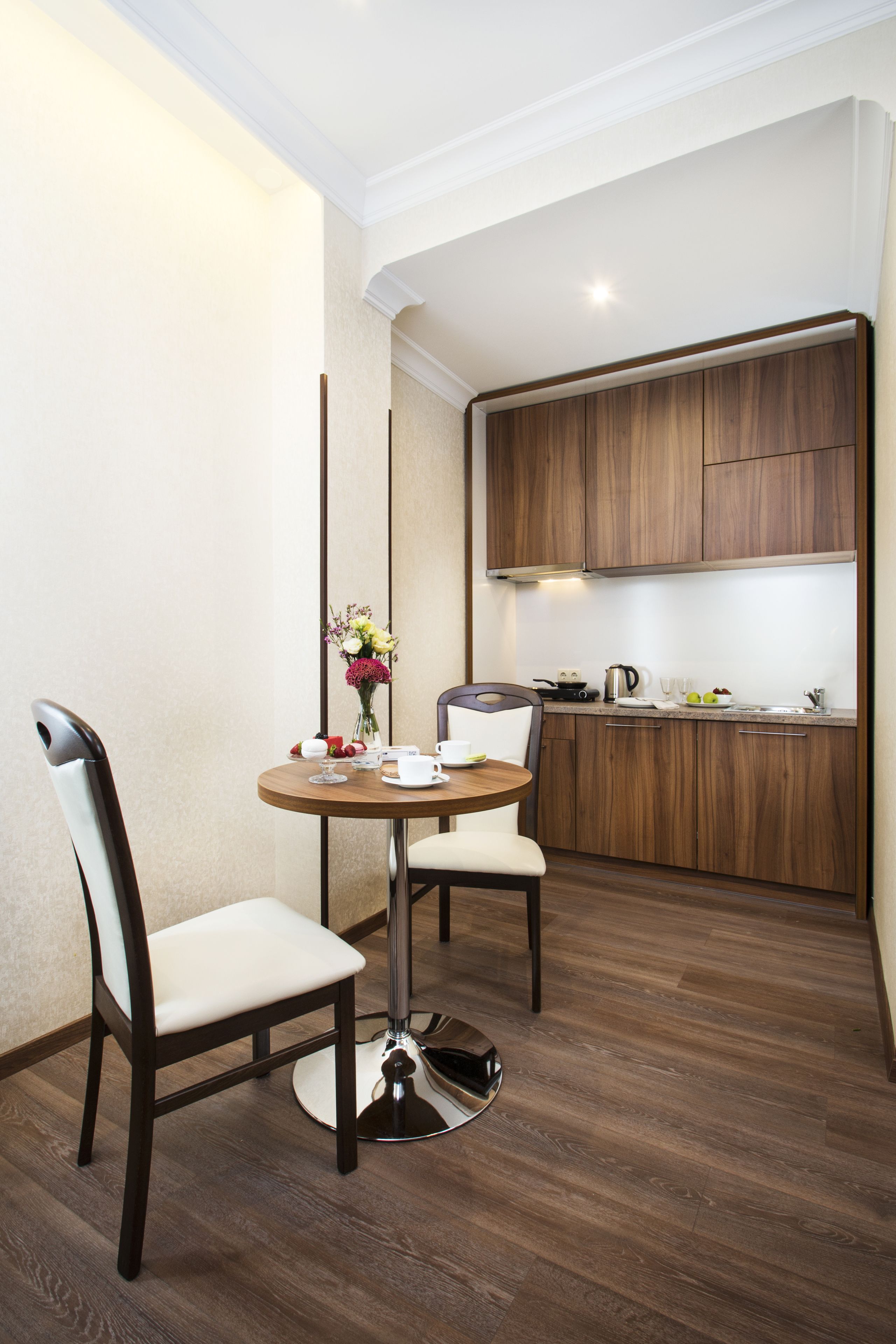 Una cocina compacta con armarios de madera, una mesa de comedor con dos sillas y un jarrón con flores.