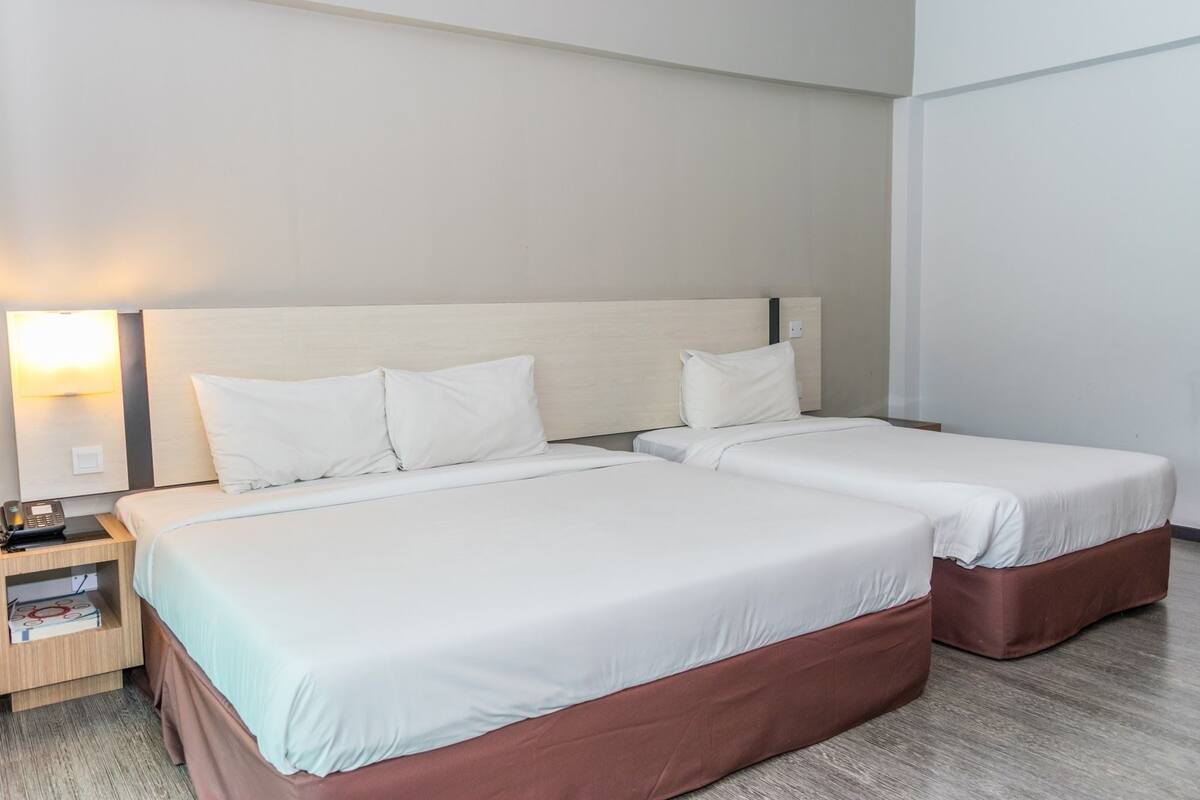 A hotel room with two beds, a nightstand with a lamp, and a wooden headboard.
