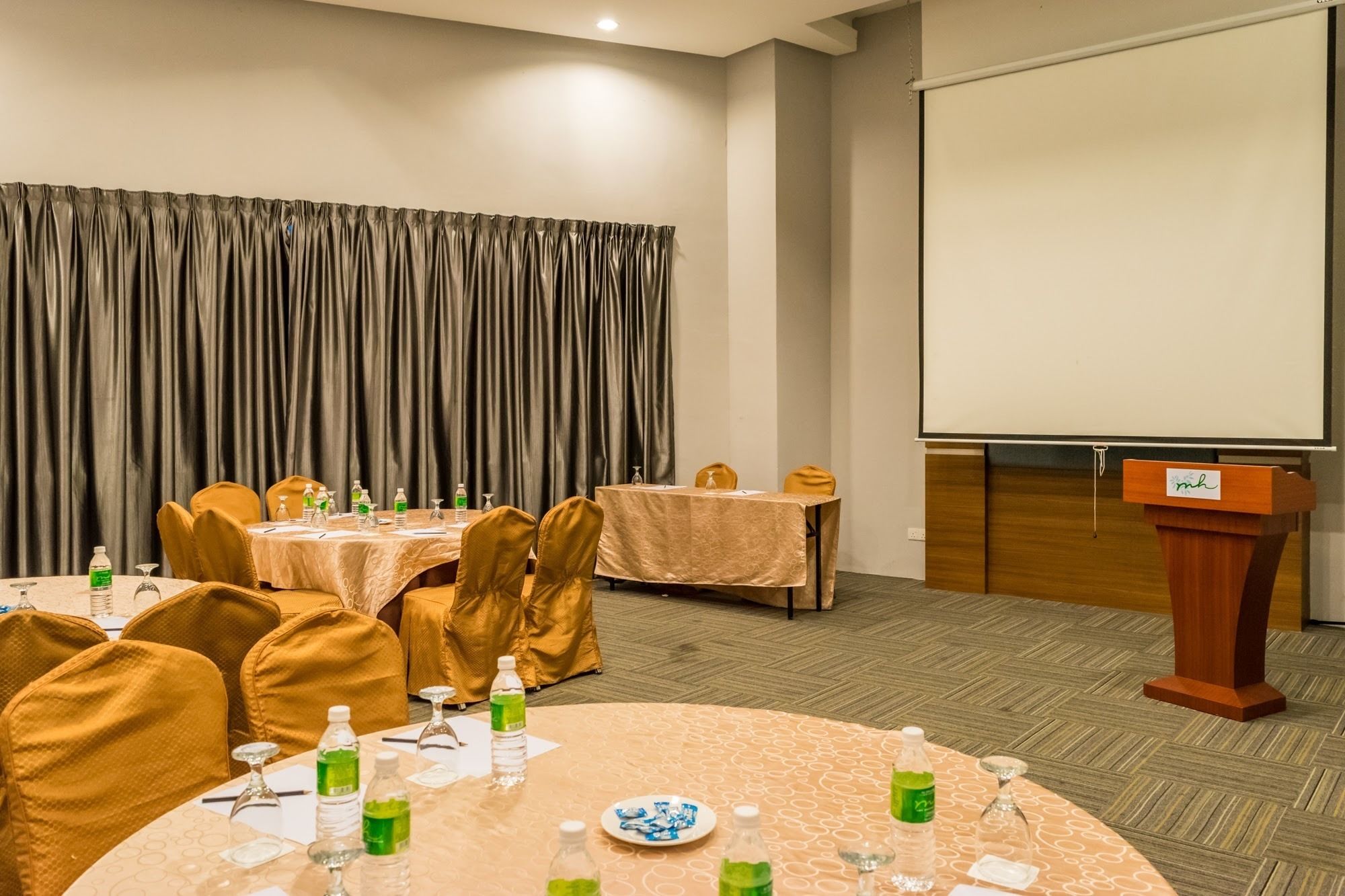 A conference room with a round table, chairs, a podium, and a projection screen.