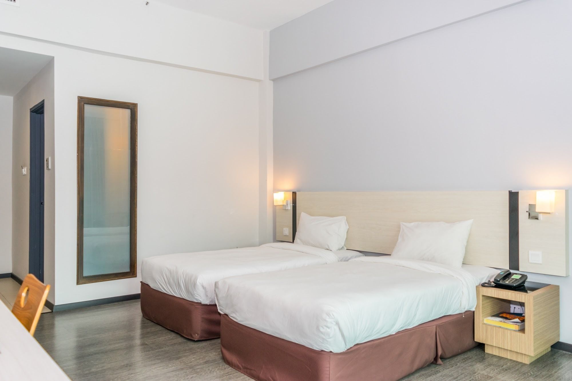 Une chambre d’hôtel avec deux lits, une table de chevet en bois avec un téléphone et un grand miroir au mur.