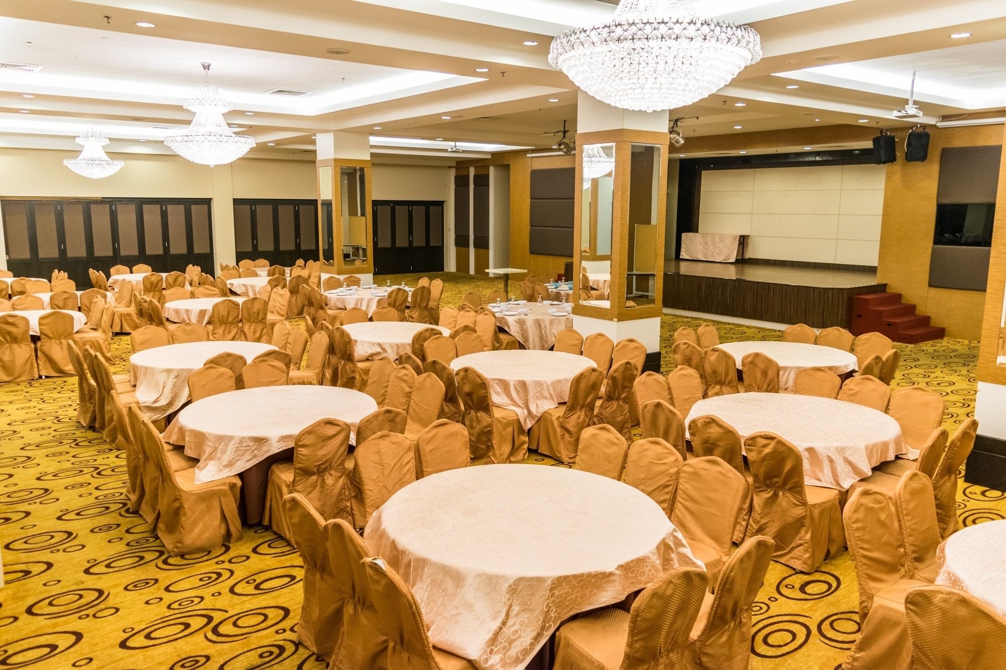 A banquet hall with multiple round tables, each surrounded by chairs with beige covers.