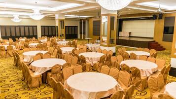 A banquet hall with multiple round tables, each surrounded by chairs with beige covers.
