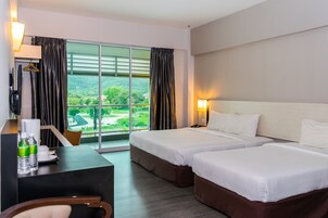 A hotel room with two beds, a desk, and a view of a green landscape.