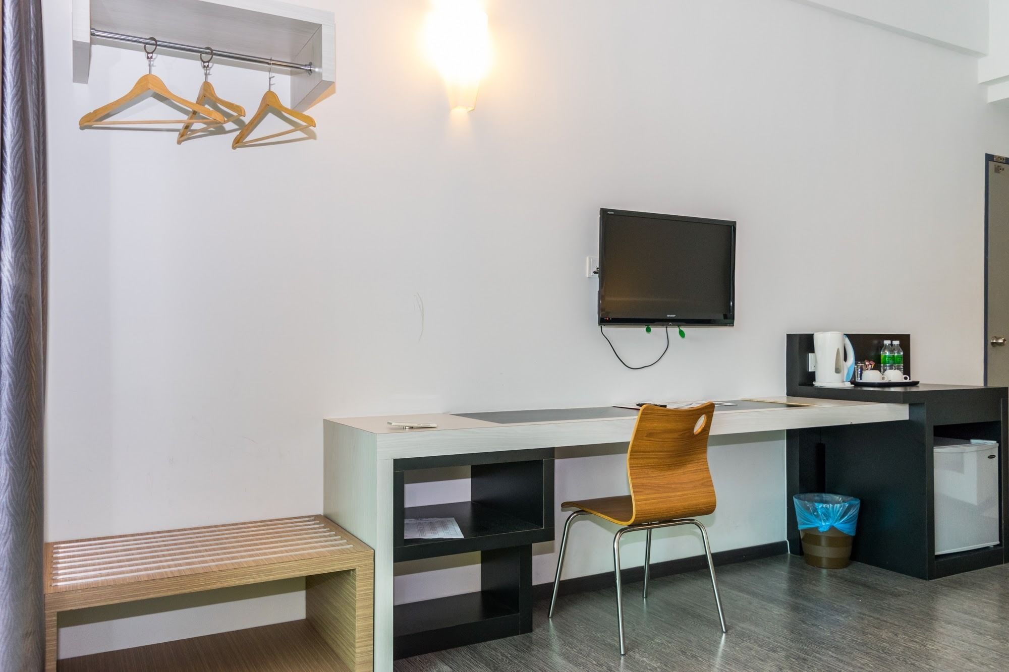 Habitación de hotel moderna con un escritorio de madera, una silla, un televisor de pantalla plana, una cafetera y un cesto de basura.
