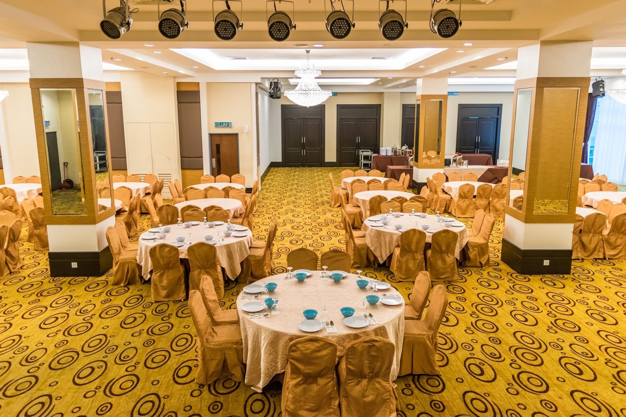 A banquet hall with round tables, chairs, and a patterned carpet.