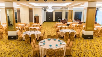 A banquet hall with round tables, chairs, and a patterned carpet.