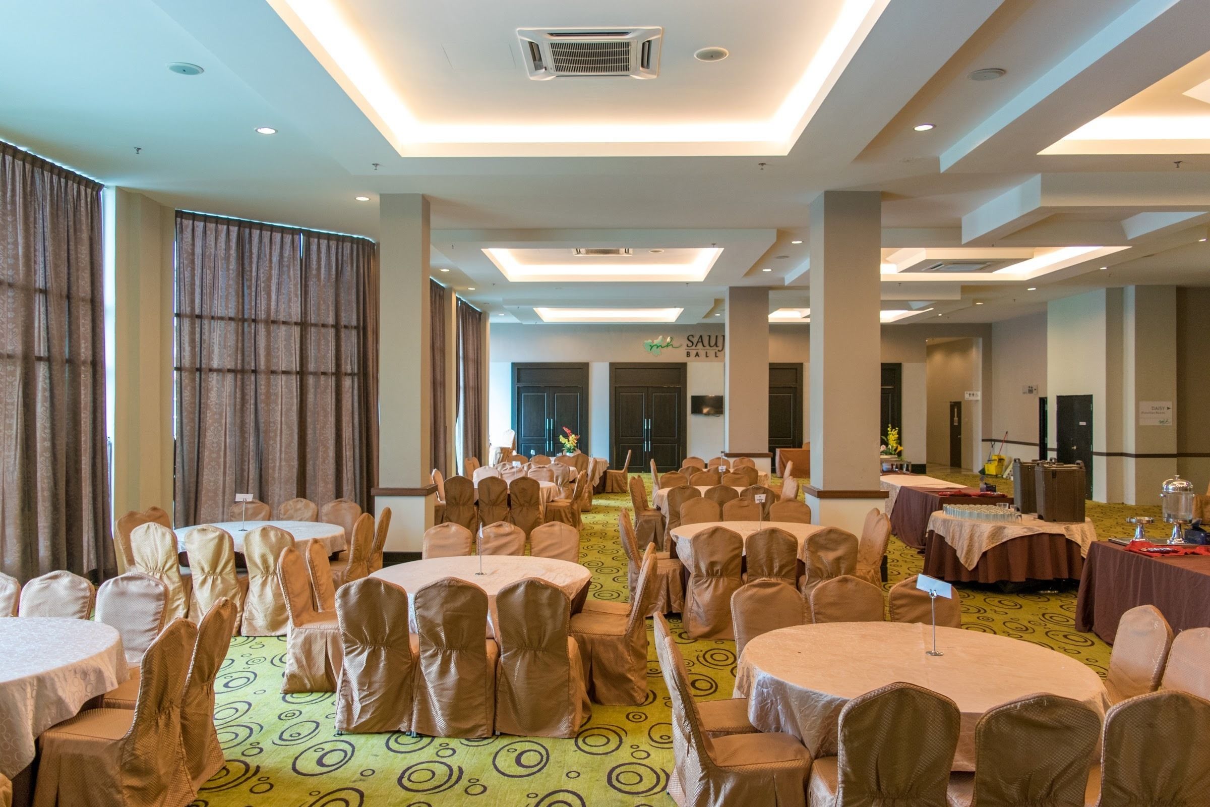 Une salle de banquet avec des tables et des chaises rondes, un sol recouvert de moquette et une enseigne indiquant « SAU BALI ».
