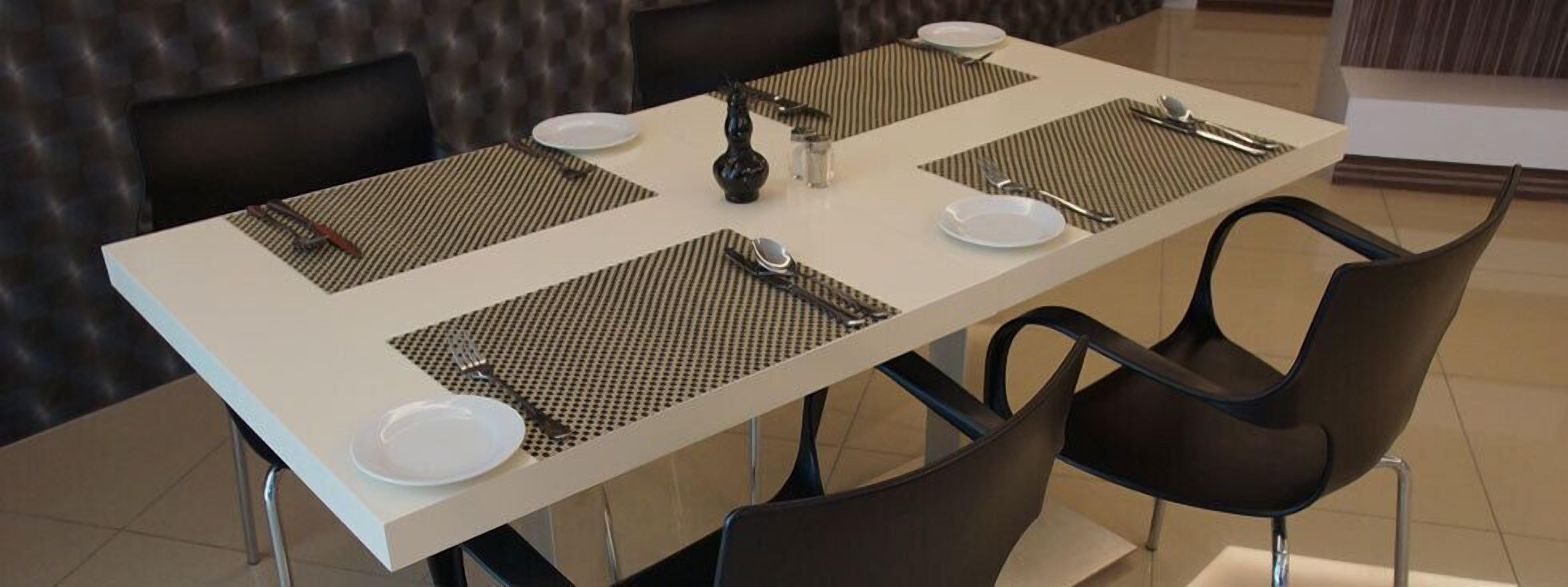 A dining table set with place settings, including plates, cutlery, and a decorative vase.