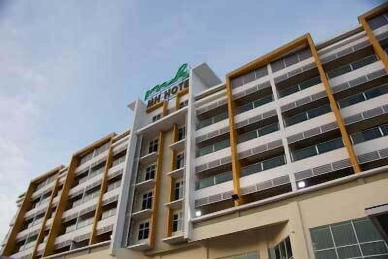 A multi-story hotel building with a modern architectural design, featuring a prominent green and white sign at the top.