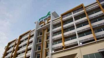 A multi-story hotel building with a modern architectural design, featuring a prominent green and white sign at the top.