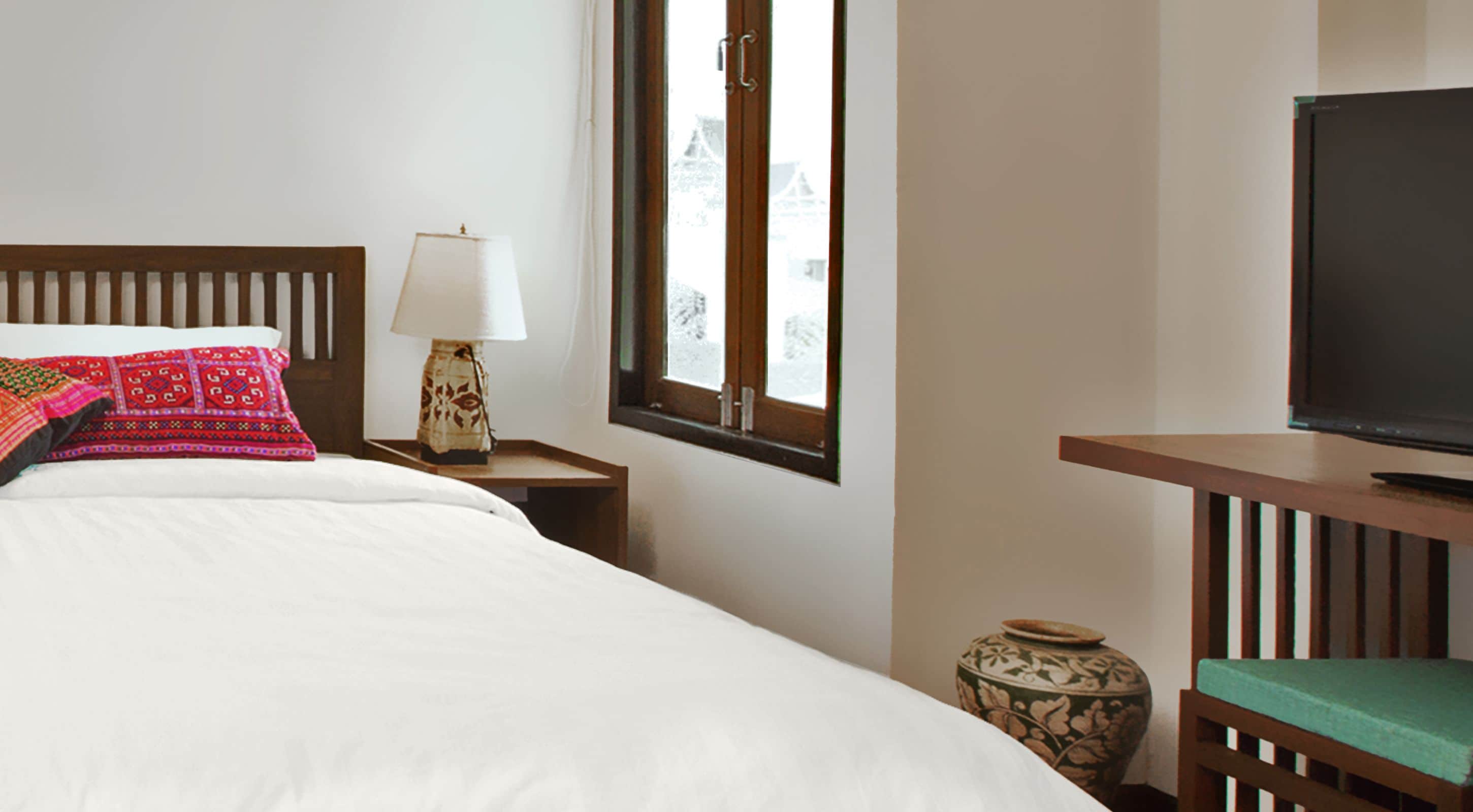 Une chambre d’hôtel avec un lit, une lampe, un téléviseur et une petite table sur laquelle se trouve un vase.
