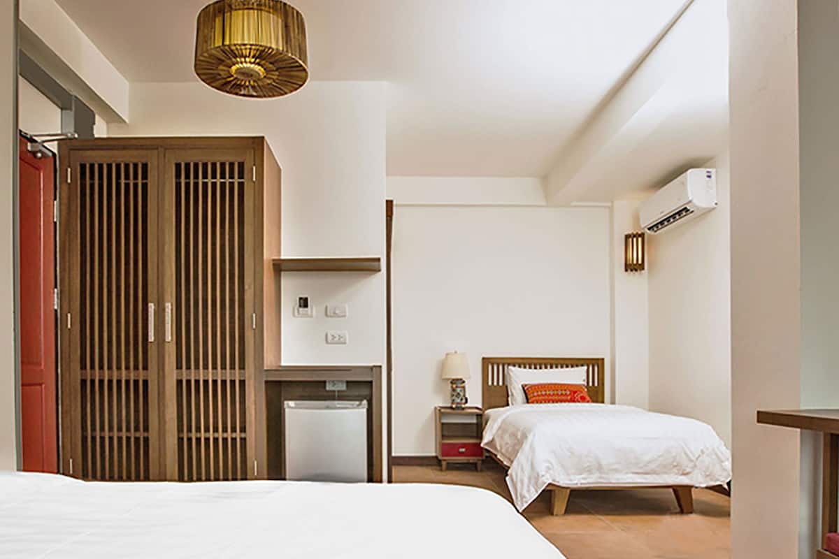 A bedroom with a bed, a desk, a wardrobe, and an air conditioning unit.