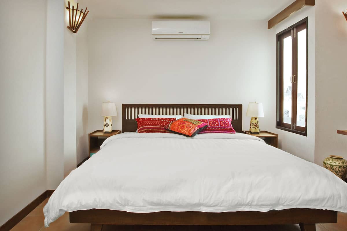 A hotel room with a bed, bedside lamps, a television, and a window.