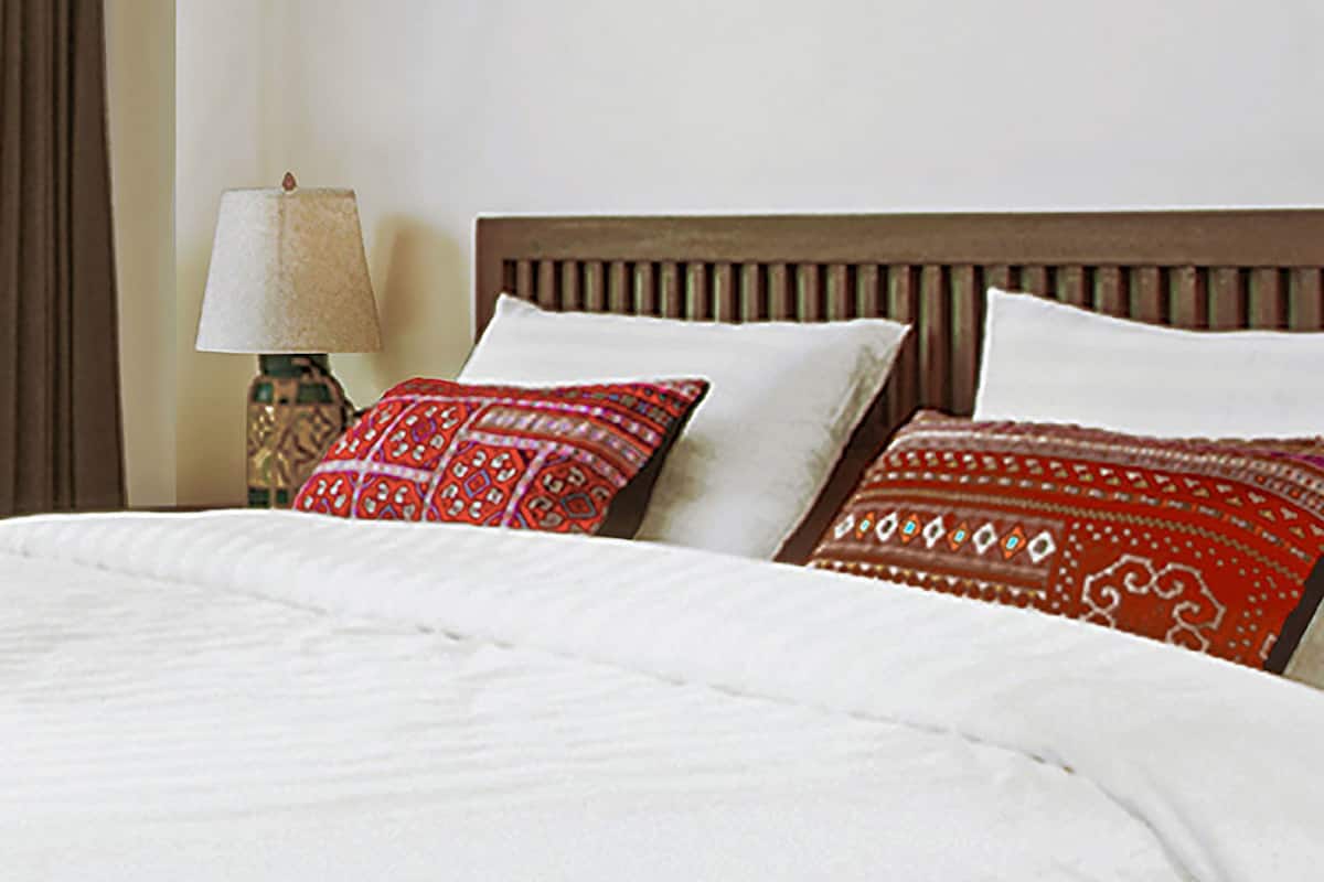 A neatly made bed with white bedding and two decorative pillows with red patterns.