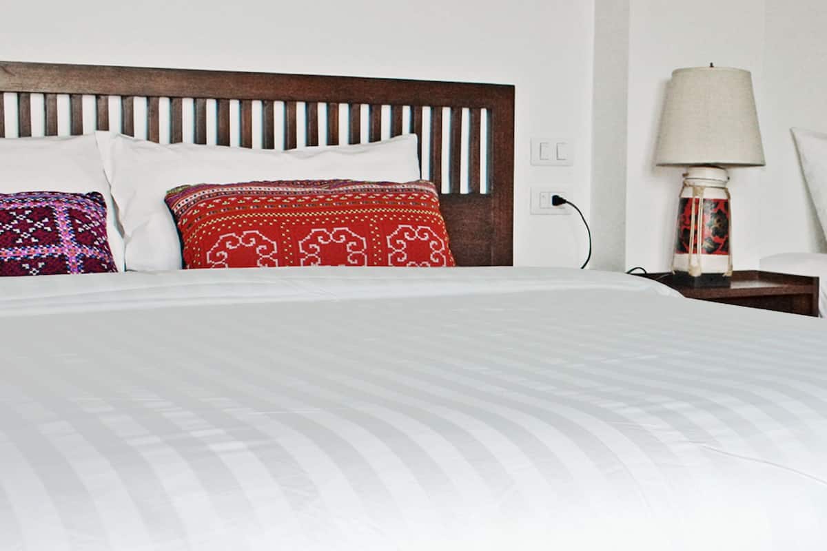 A hotel room with a large bed, two pillows, a nightstand with a lamp, and a wall socket.