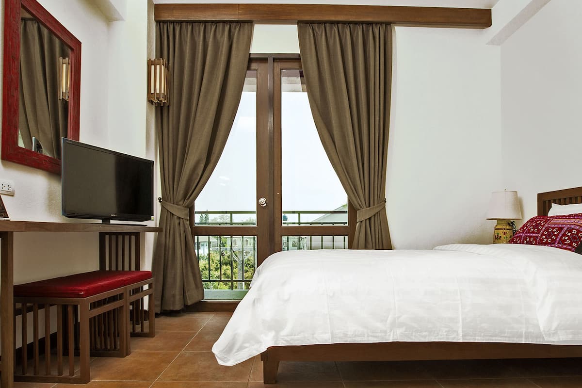 A hotel room with a bed, a TV, a desk with a chair, and a balcony with curtains.