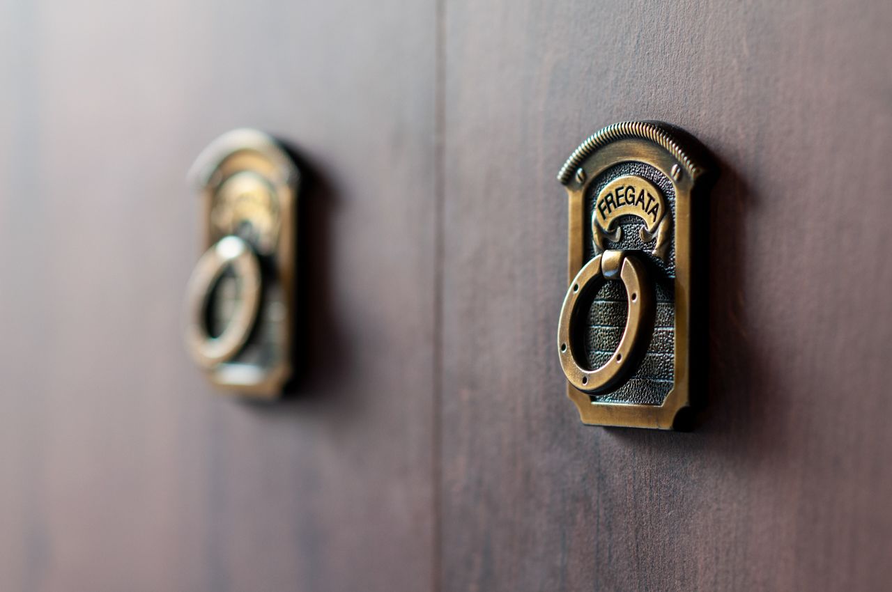 Deux heurtoirs de porte en laiton, portant le mot « FREGATA », sur une porte en bois.