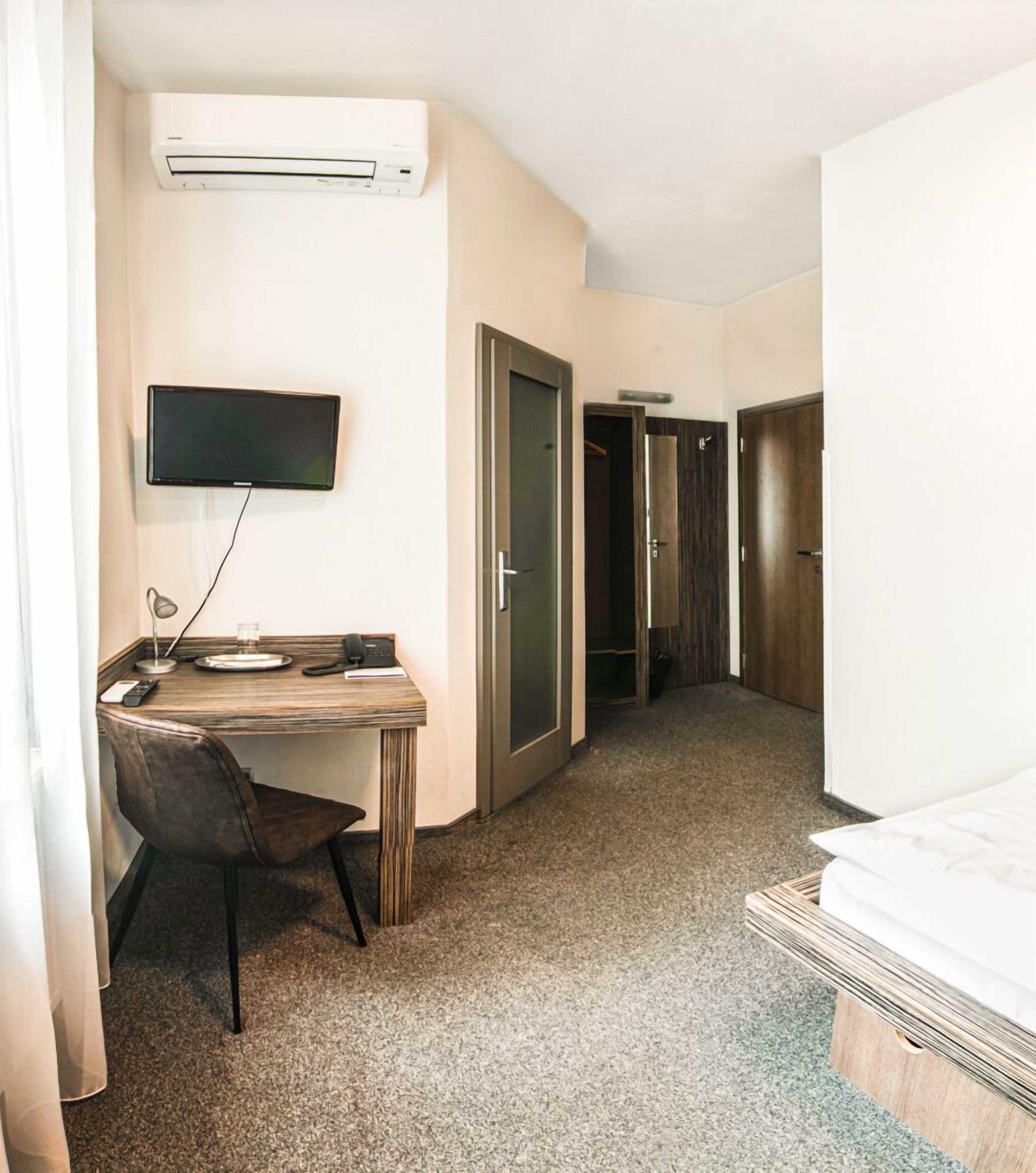 Habitación de hotel con escritorio, silla, televisor, aire acondicionado y cama.