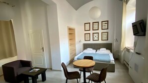 Een moderne hotelkamer met een bed, een ronde tafel met stoelen, een bank, een aan de muur bevestigde televisie en een plafondlamp.