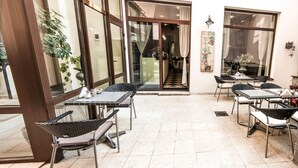 Een ruim buitgedeelte met tafels en stoelen, grote ramen en uitzicht op het interieur.