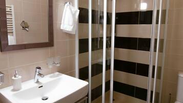 Une salle de bain moderne avec une douche à parois courbes en verre, un lavabo blanc avec un miroir et des toilettes.