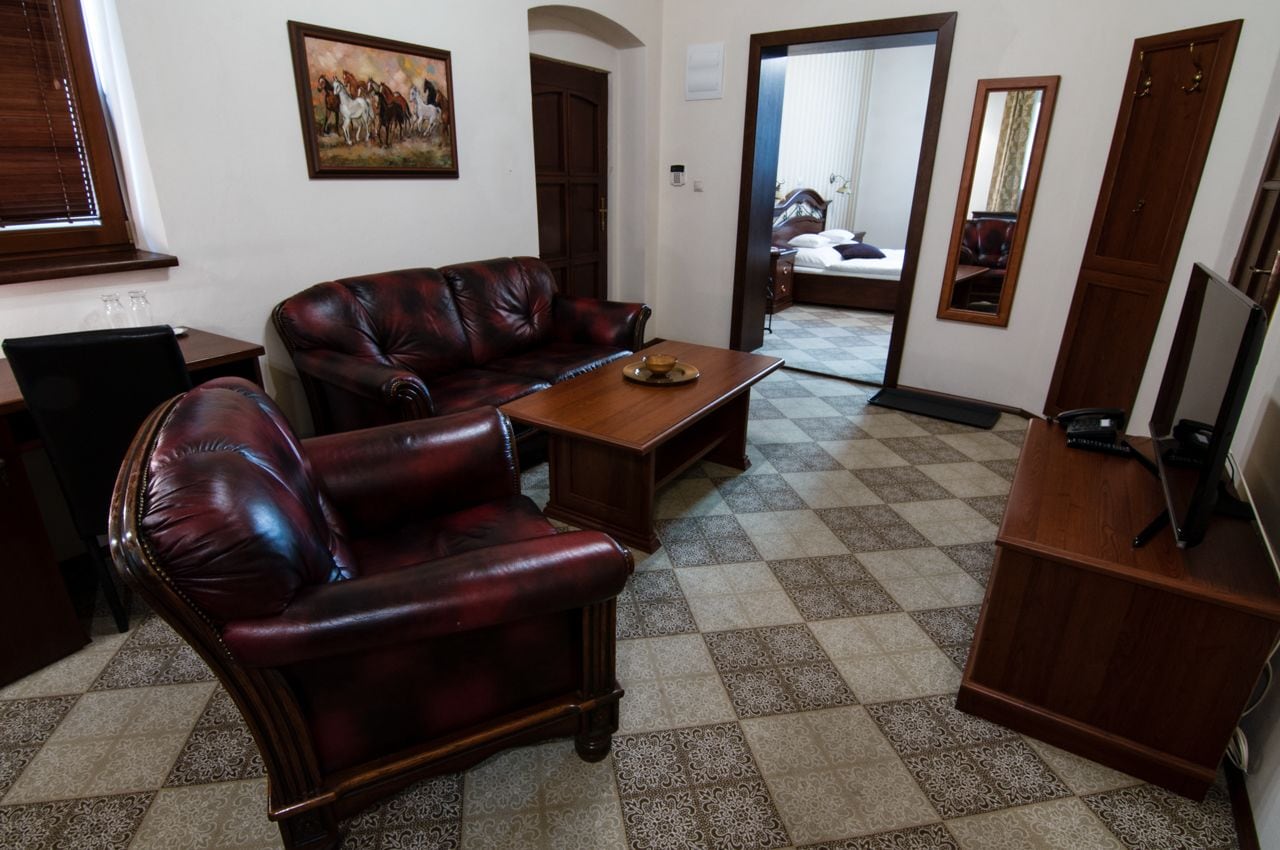 Una habitació amb un terra de pissos, un sofà de pell, una taula de centre de fusta, un televisor sobre un suport de fusta i un quadre a la paret.