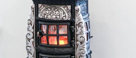 Una estufa decorativa con ornamentación metálica detallada y una puerta de vidrio, mostrando un fuego visible en su interior.