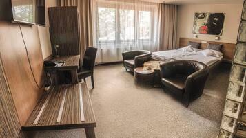 A hotel room with a bed, a desk, a chair, a sofa, and a TV.