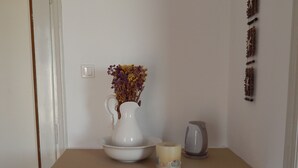 A kitchenette with a white refrigerator, a white kettle, and a white pitcher with dried flowers.