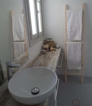 A bathroom with a large oval sink, wooden towel racks, a window, and a mirror.