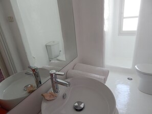 A bathroom with a white sink, a mirror, a toilet, and a shower curtain. - Hotel Helmos (Naxos)