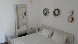 A bedroom with a bed, a mirror, a wall clock, a wall-mounted lamp, and two hats.