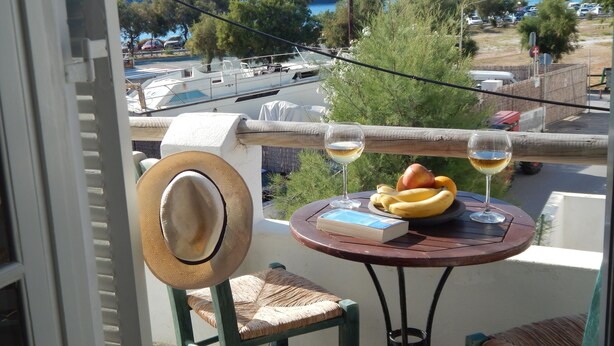 A balcony with a table, two chairs, a hat, a book, and two glasses of wine.
