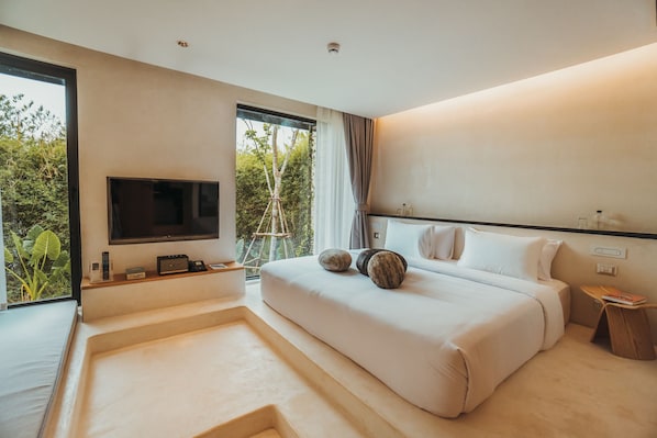 Una habitación de hotel moderna con una cama grande, un televisor montado en la pared, una mesita de noche pequeña y una ventana con vistas a zonas verdes.