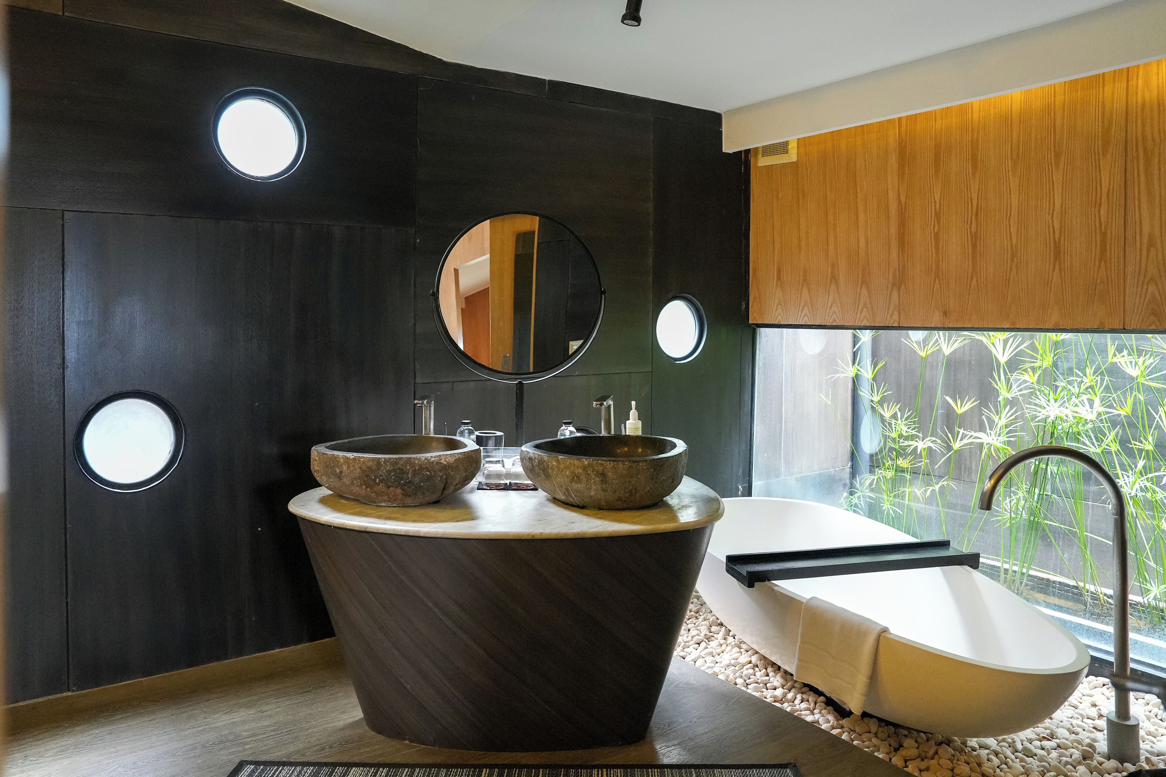A modern bathroom with a freestanding bathtub, two stone sinks, and a large mirror.
