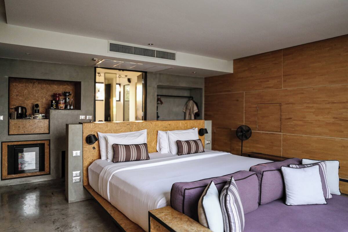 Ein modernes Schlafzimmer mit einem großen Bett, einem Holzkopfteil und einer eingebauten Nische mit Küchengeräten.
