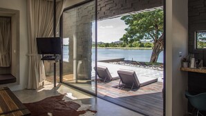 Una habitación moderna con un amplio ventanal corredero que da a una terraza con mobiliario exterior y vistas a un lago.