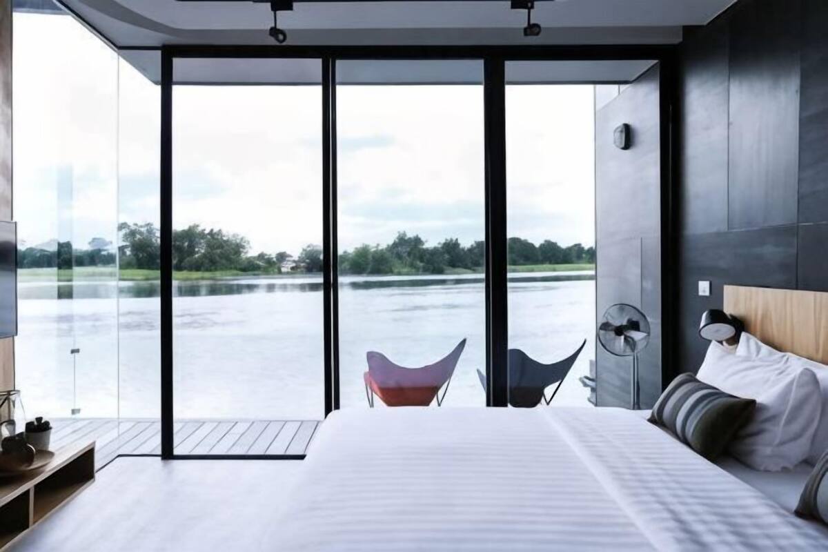 Ein modernes Schlafzimmer mit einem großen Bett, einem Sessel und Seeblick durch große Glasfenster.