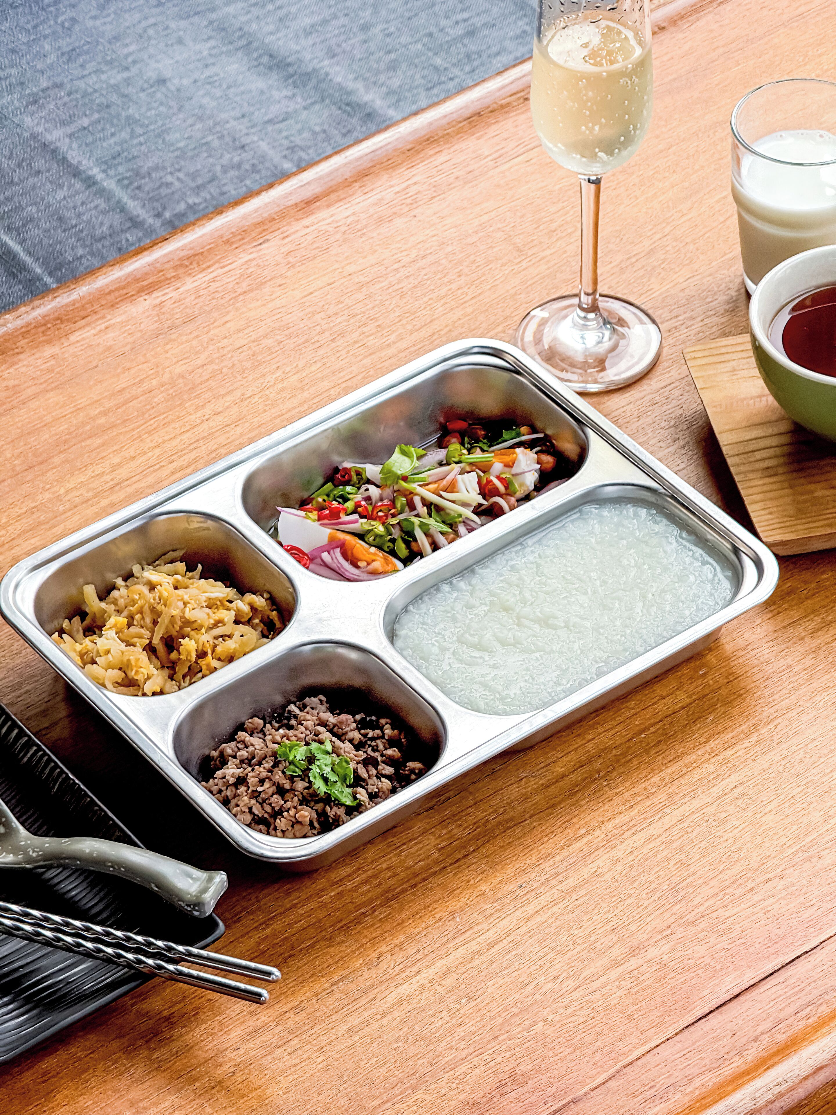 A meal tray with various food items and a glass of white wine on a wooden table.