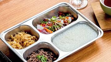 A meal tray with various food items and a glass of white wine on a wooden table.