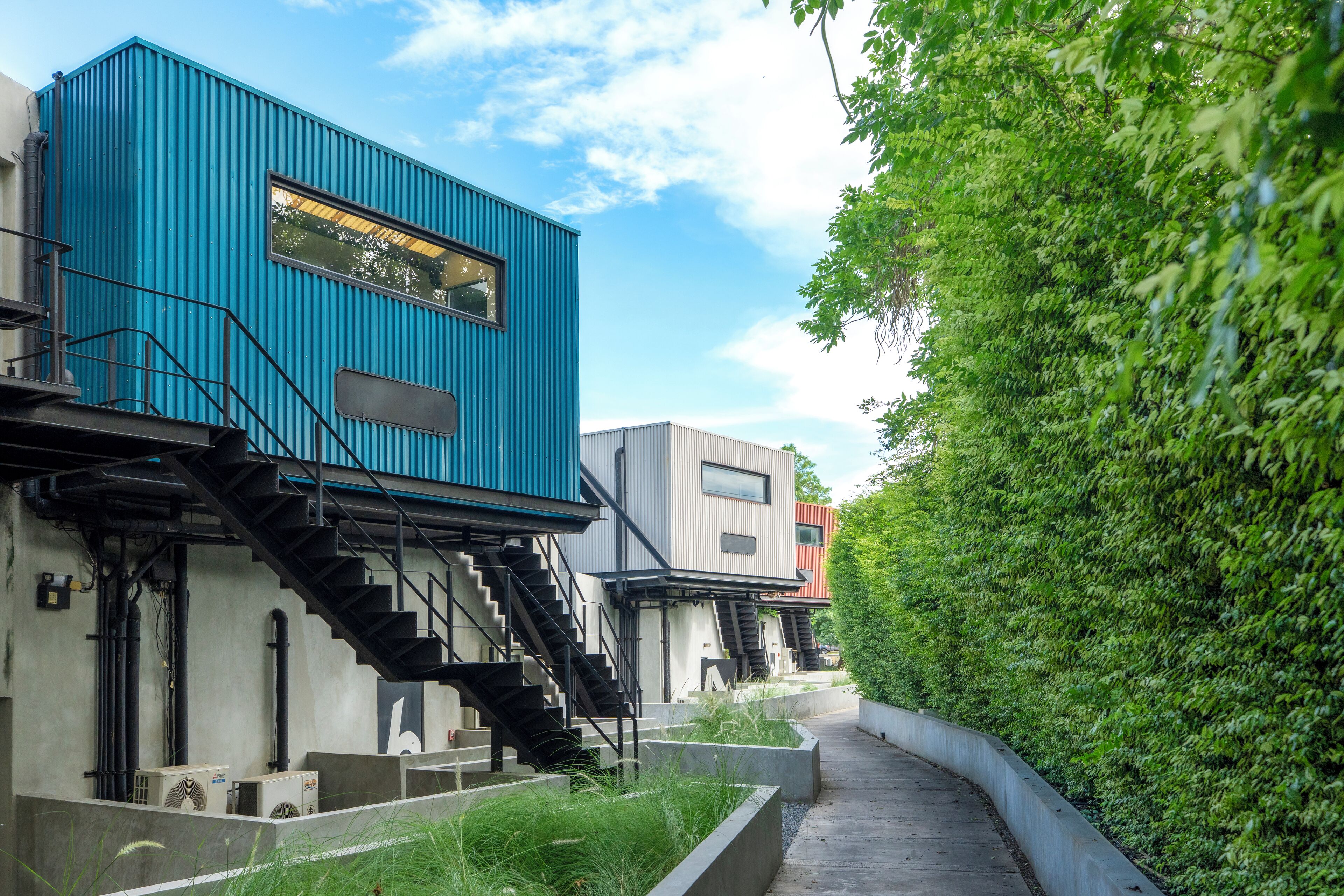 Un edificio moderno con fachada azul, una escalera y un camino al lado de un seto verde.